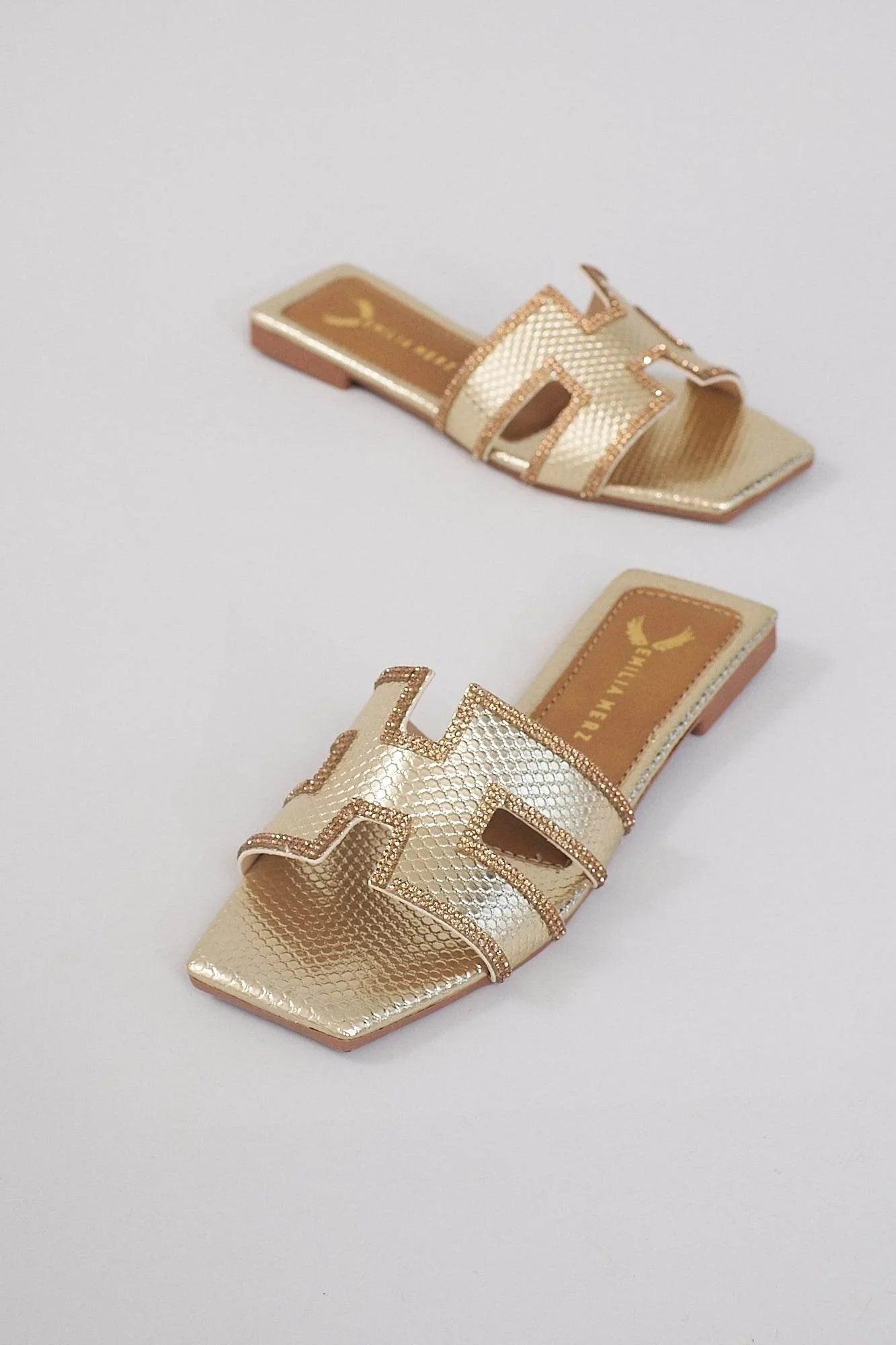 Gold slip-on sandals with textured leather and open toe design on a light background.