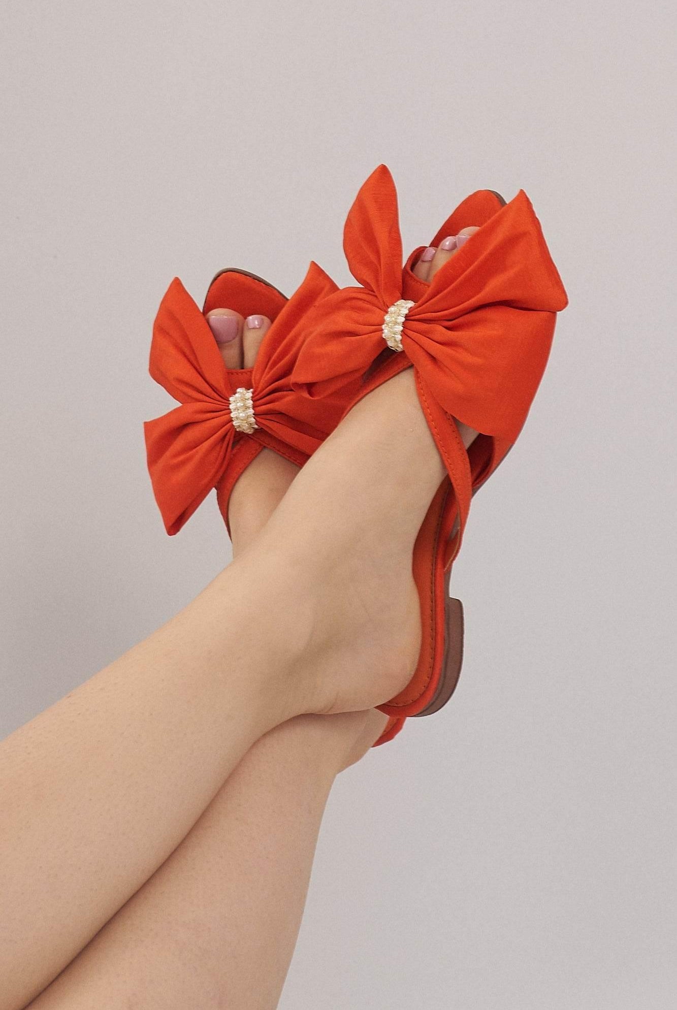 Woman wearing orange ribbon flats with pearl detail against neutral background