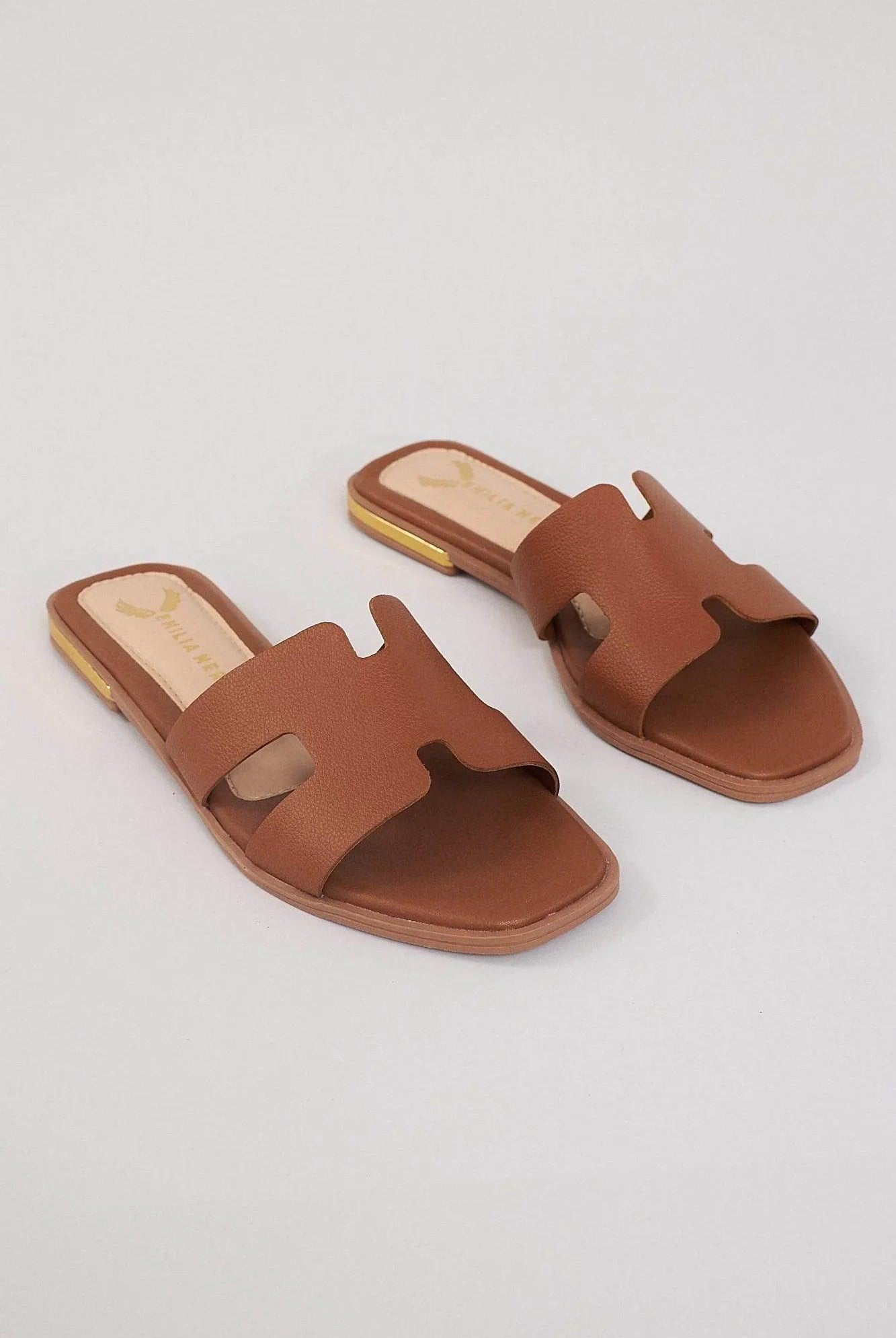 Brown leather slides with cutout design and square toe on a neutral background