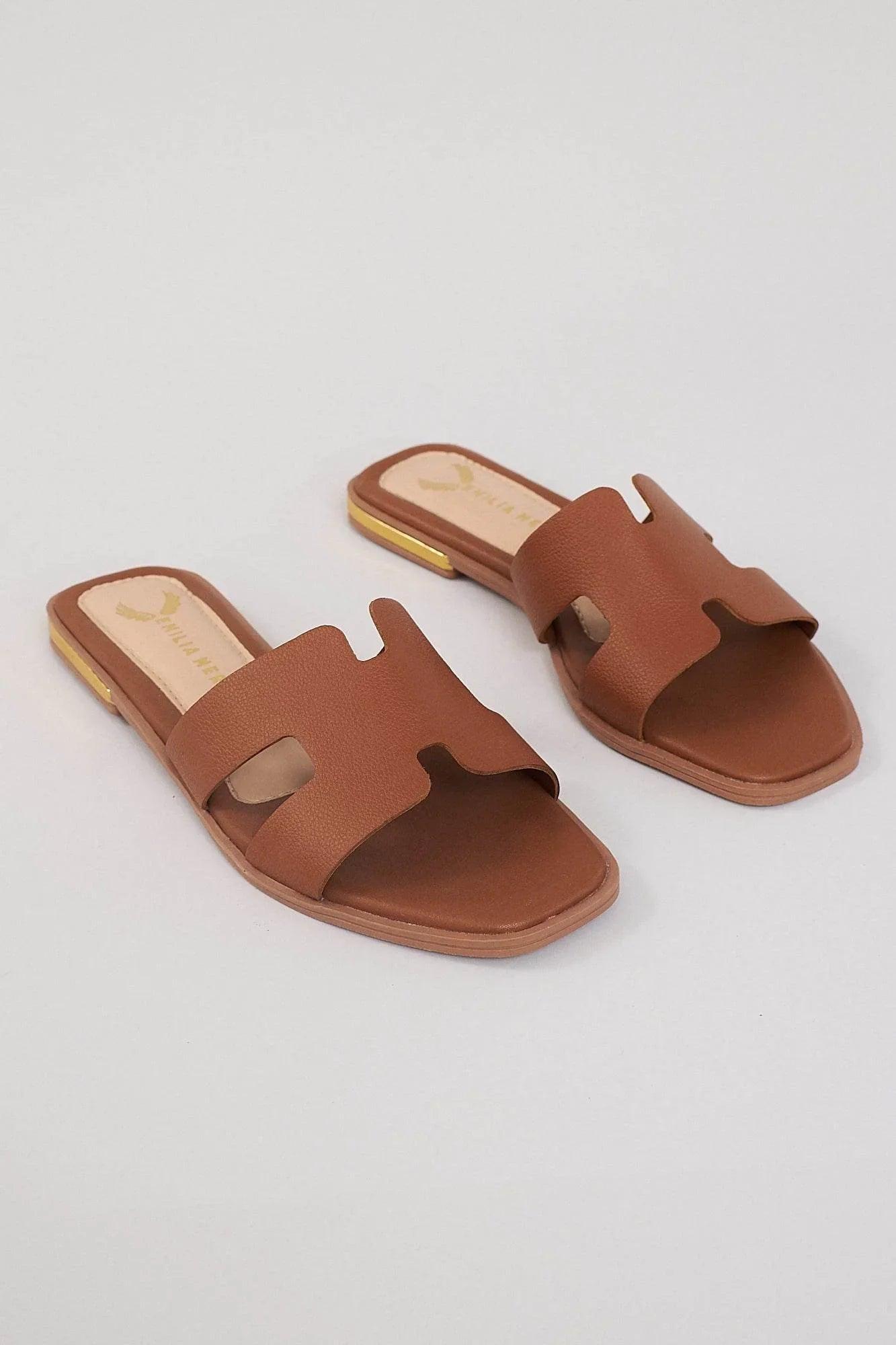 Brown leather slides with cutout design and square toe on a neutral background