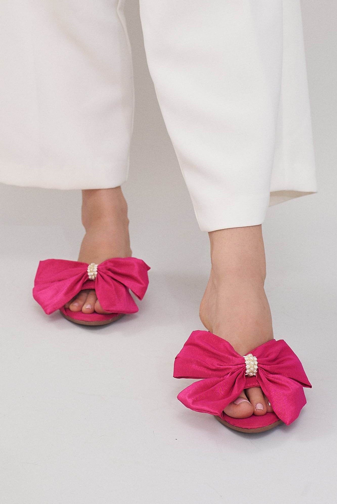 Woman wearing pink sandals with large bows and pearl accents, paired with white pants