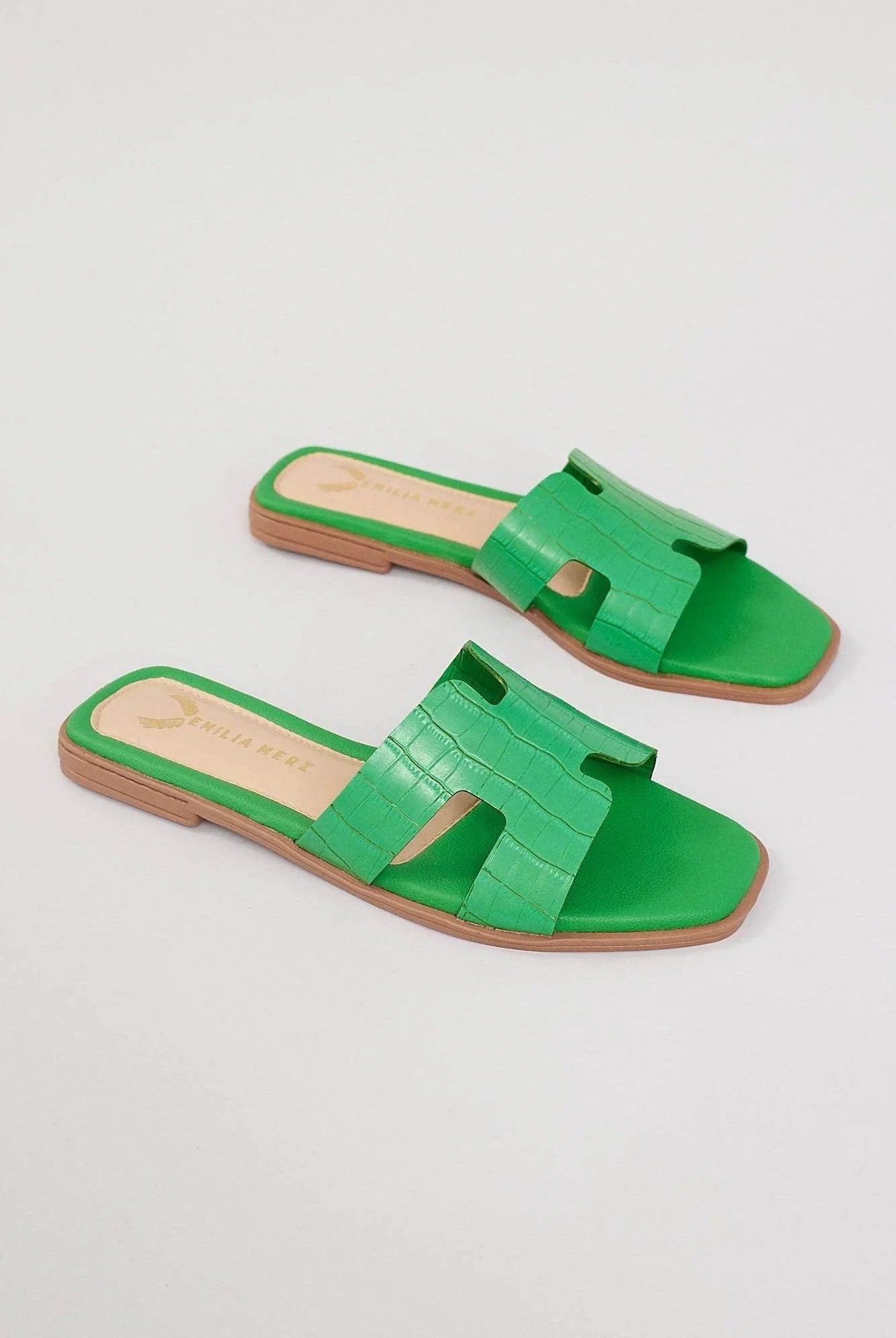 Green crocodile-texture mules with open toe and flat tan sole on white background