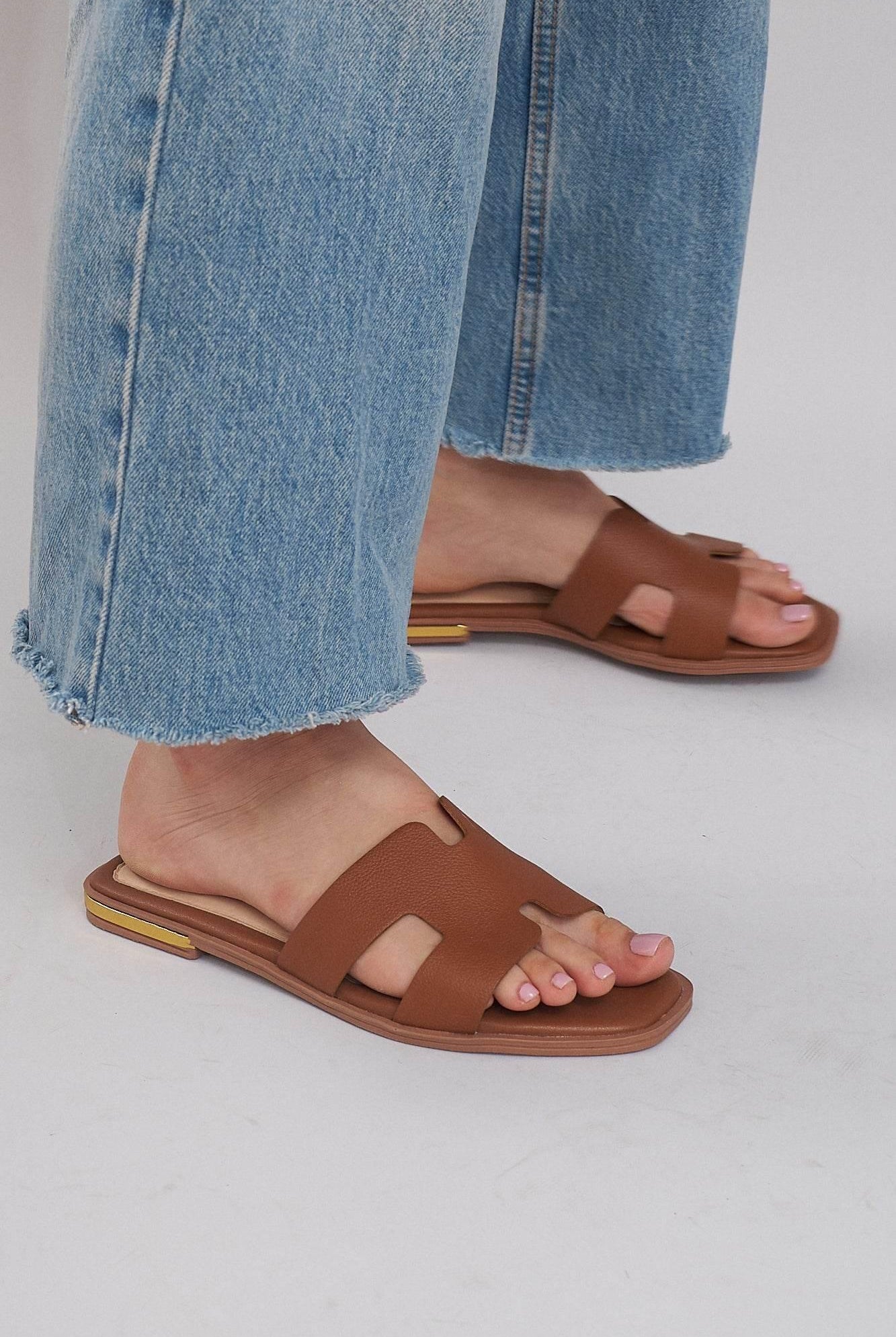 Brown leather summer slide sandals with cutout design, worn with cropped blue jeans on light floor