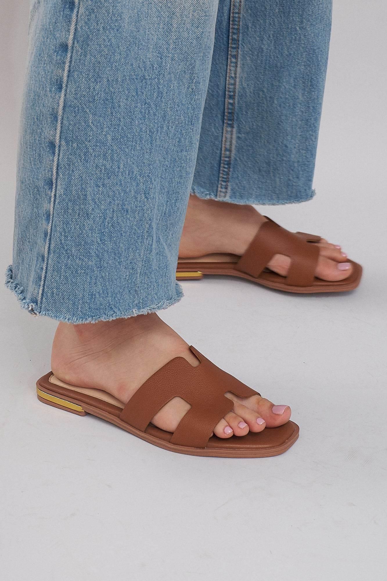 Brown leather summer slide sandals with cutout design, worn with cropped blue jeans on light floor