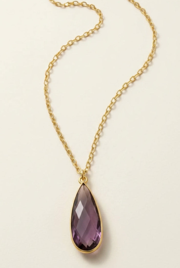 Golden aurea drop necklace with purple gemstone on a beige background