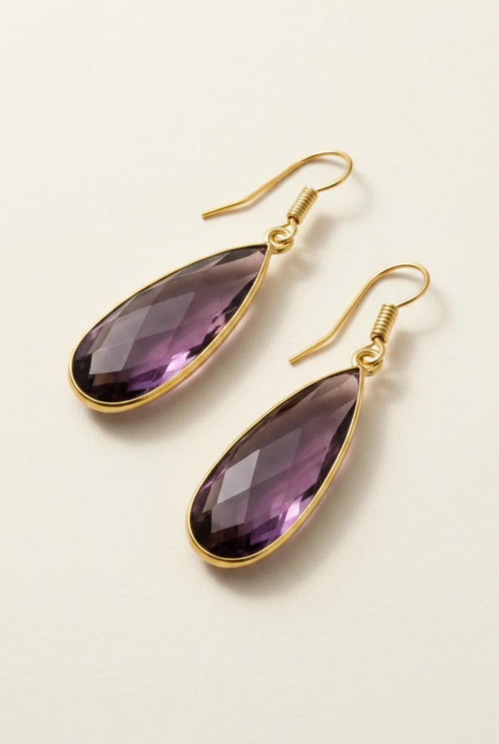 Gold aurea drop earrings with deep violet gemstones on a beige background