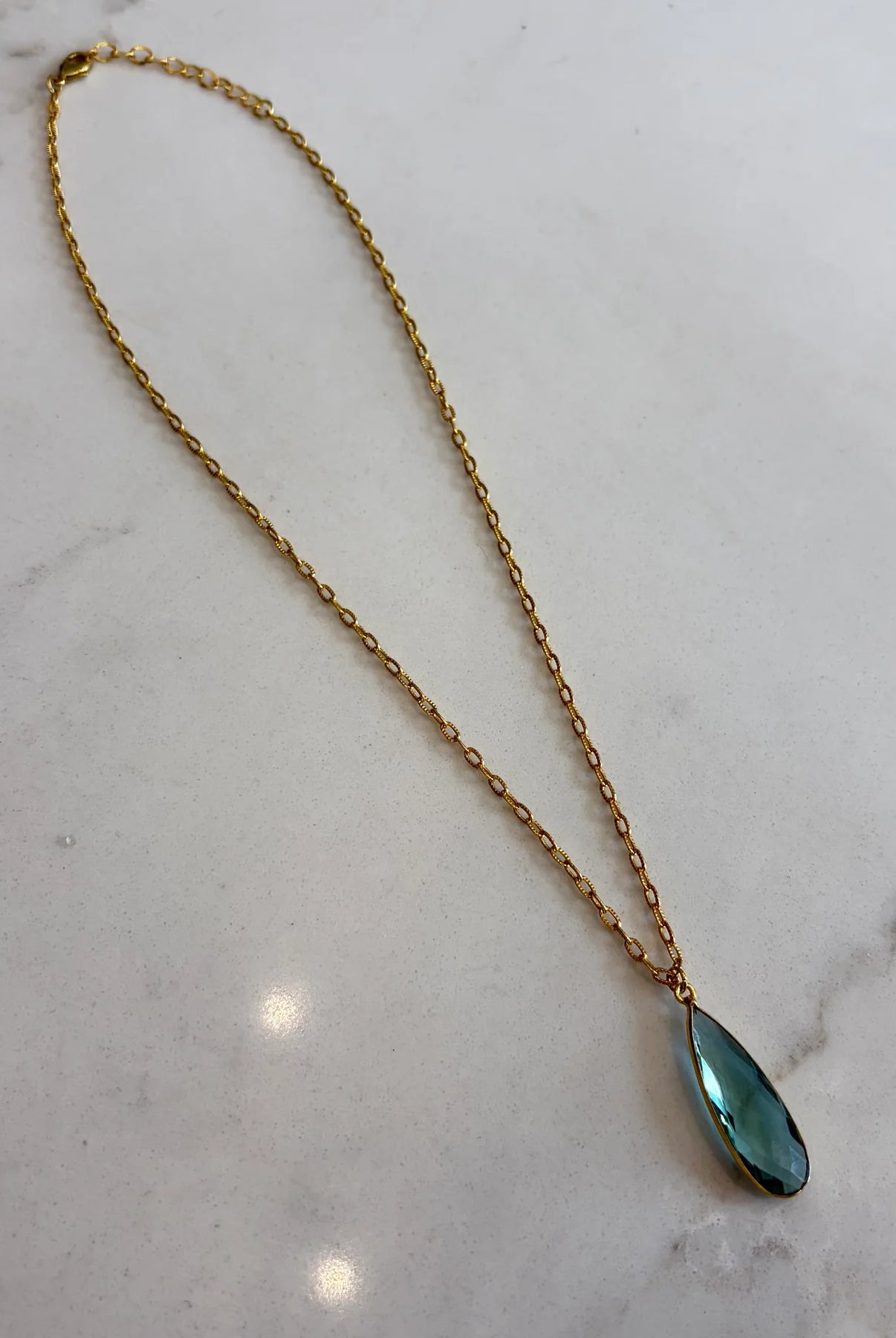 Gold necklace with a green teardrop pendant on a marble surface