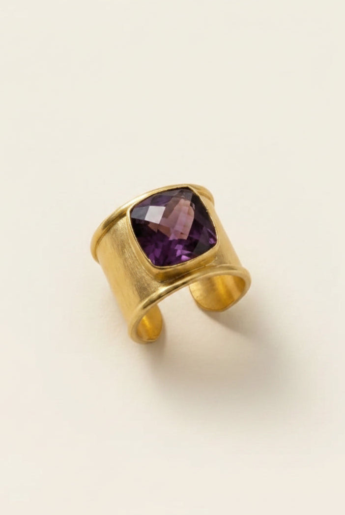 Gold aurea ring with deep violet gemstone on a beige background