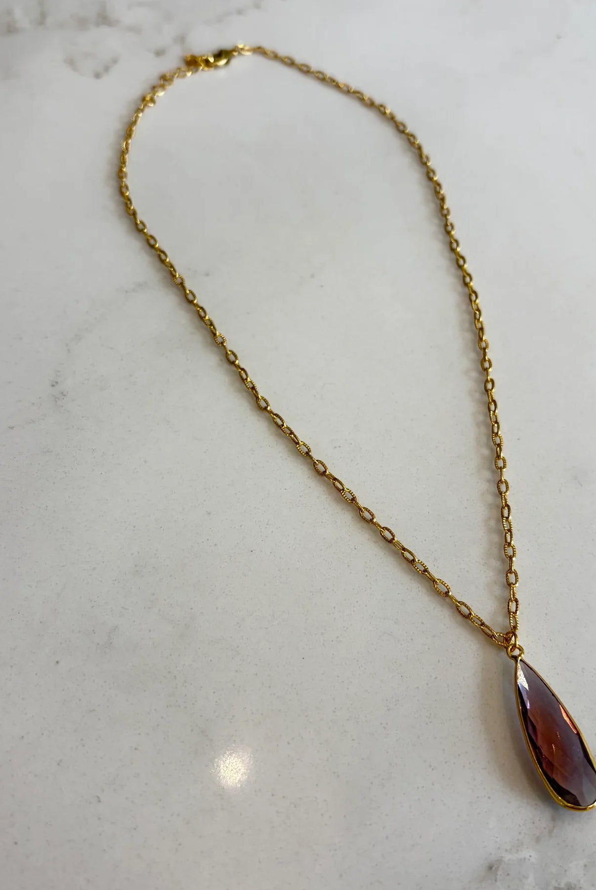 Emilia Merz Aurea pendant necklace featuring a deep violet teardrop-shaped faceted stone set in 18K gold plating on a delicate chain.