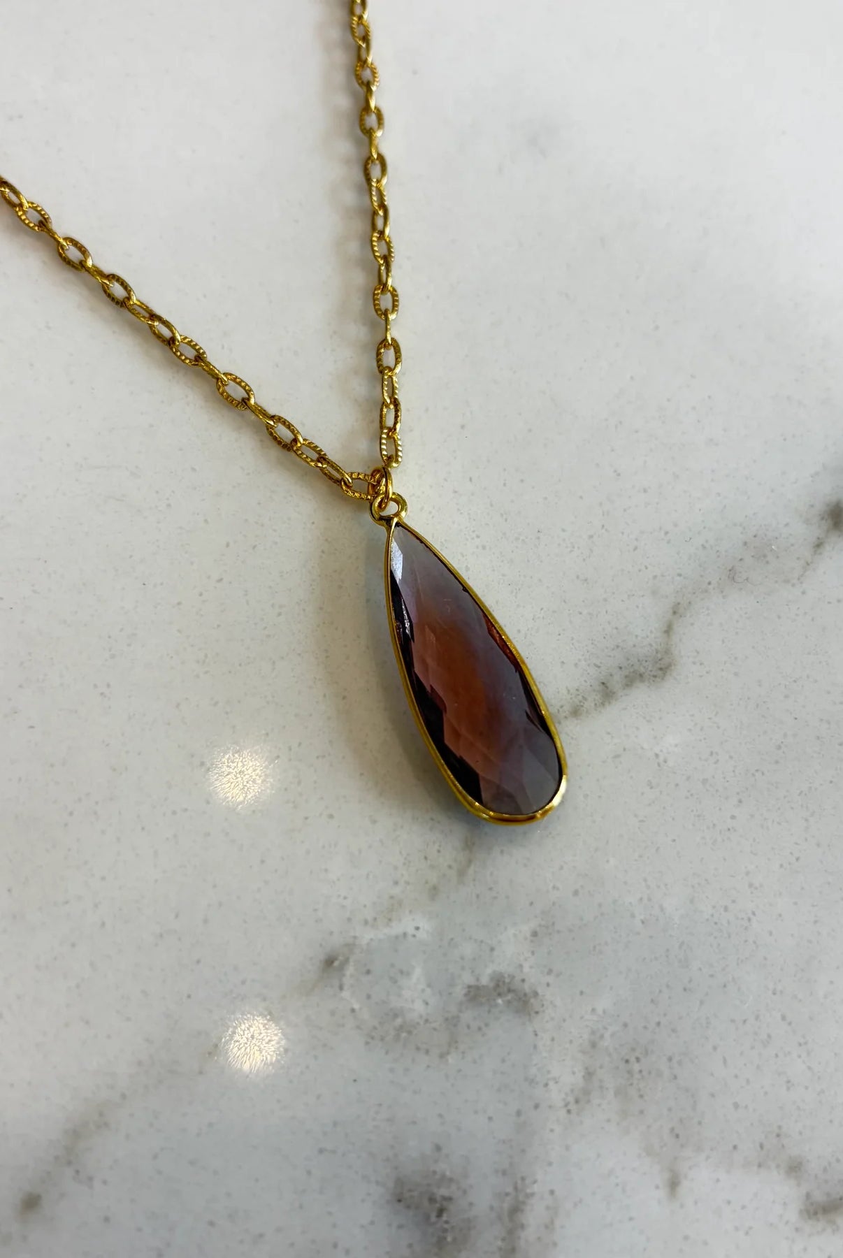 Close-up of the Aurea deep violet pendant necklace, highlighting the detailed facets of the gemstone and the polished gold setting.