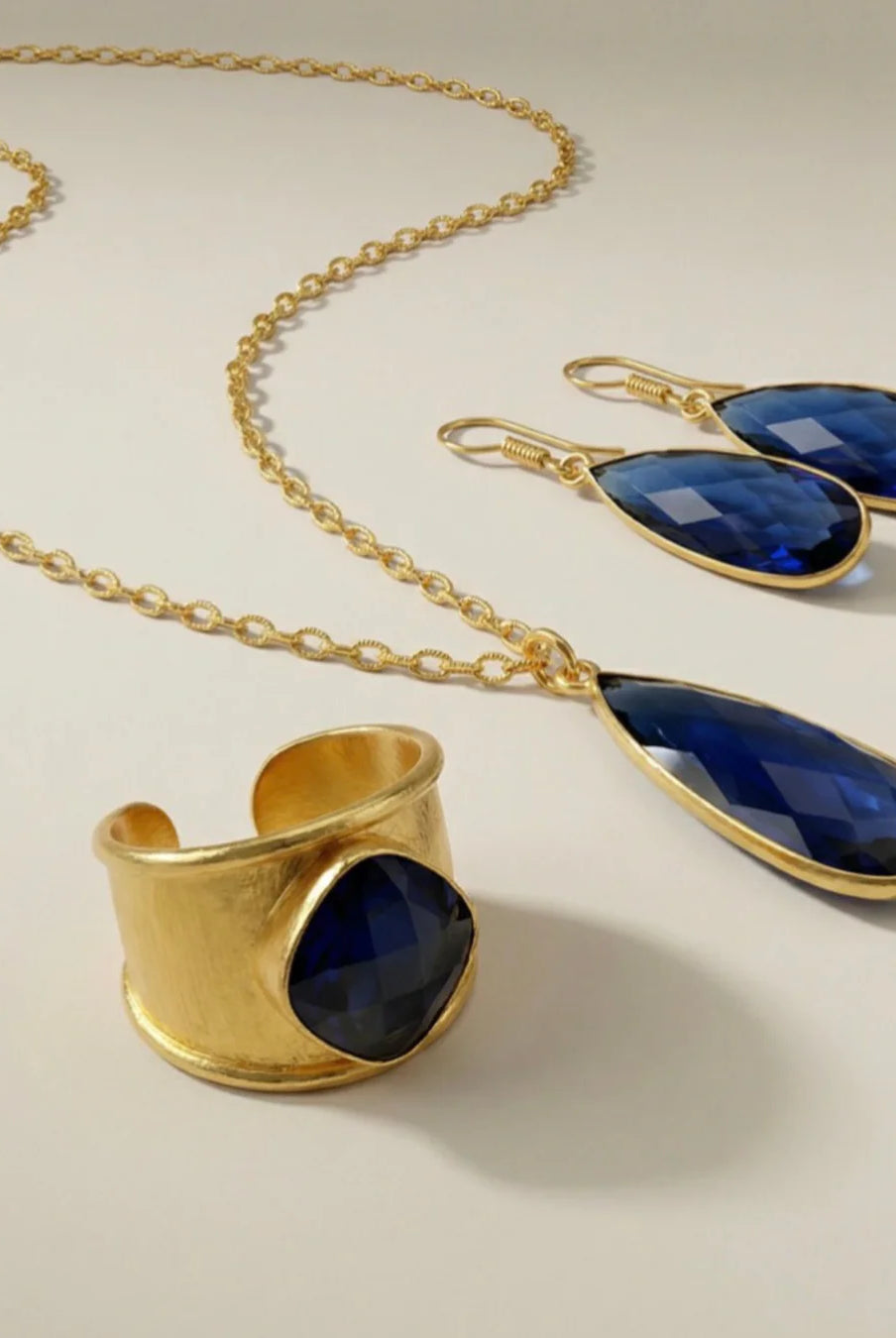 Gold jewelry Aurea set with blue stones on a beige background from emilia merz