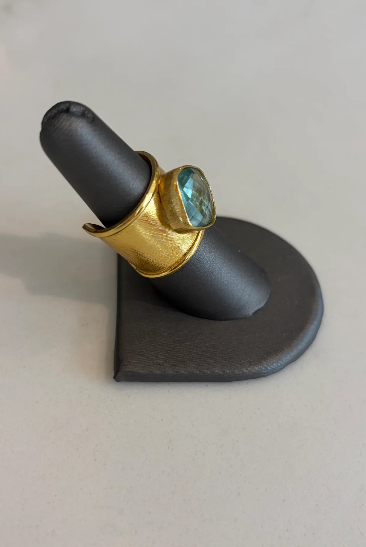 Close-up of the Emilia Merz Aurea Soft Teal statement ring, highlighting the wide, textured 18K gold-plated band and the beautiful faceted center stone.