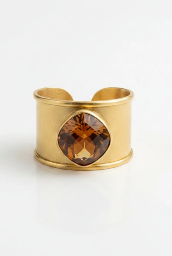 Close-up of the Emilia Merz Aurea Golden Amber statement ring on a display stand, highlighting the wide, textured 18K gold-plated band and the beautiful faceted center stone.