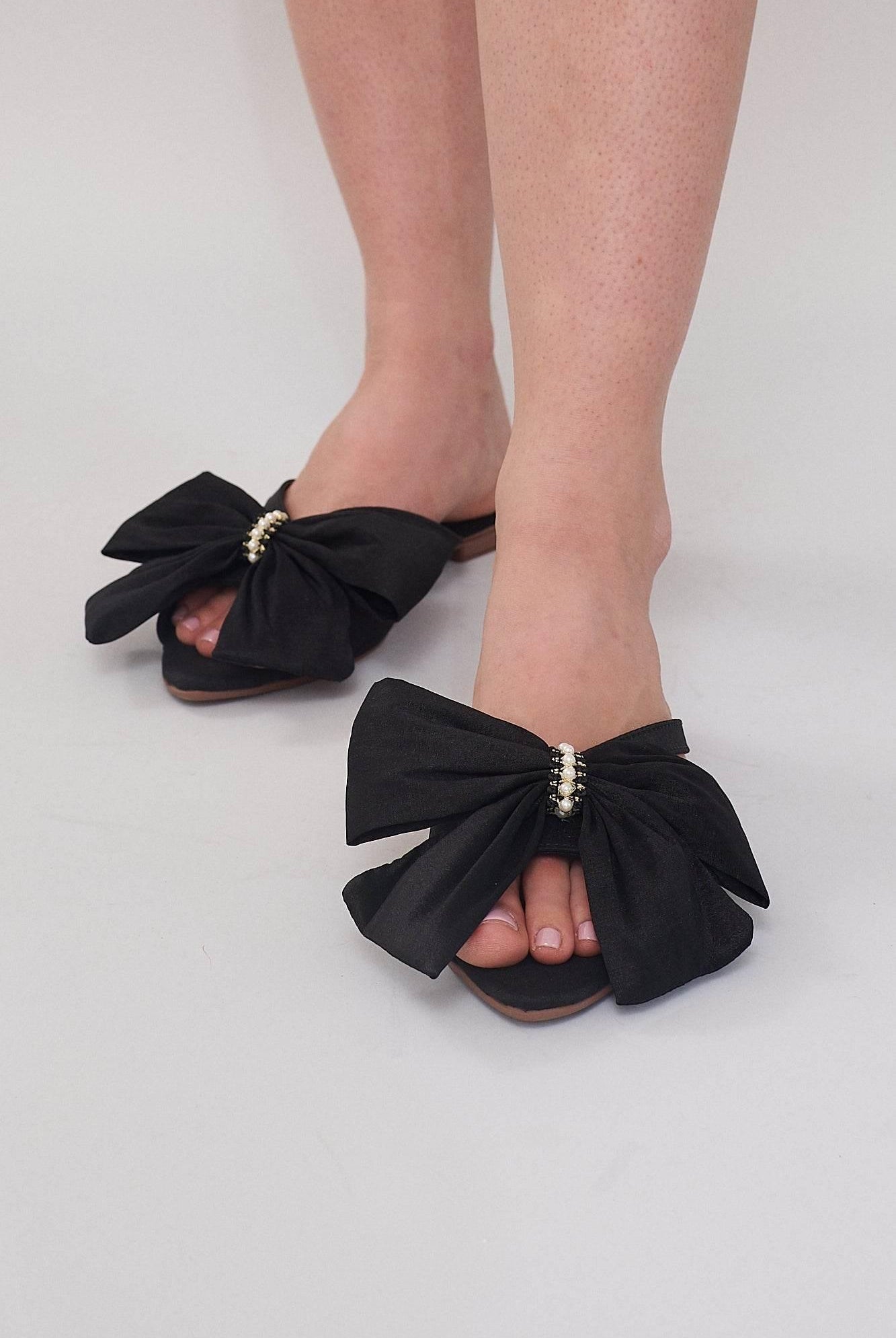 Comfortable black flat sandals for women with statement bow and pearl detailing.
