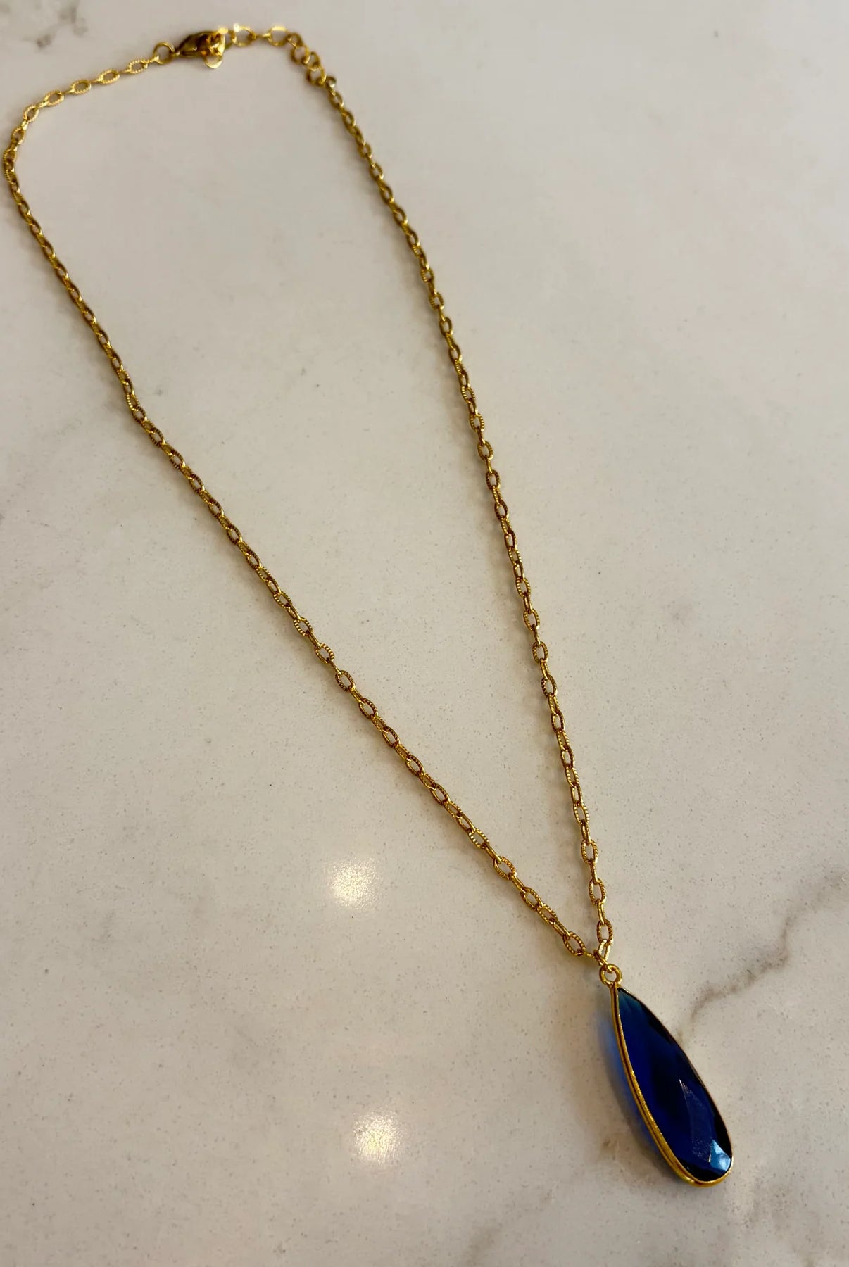 Gold necklace with a blue pendant on a marble surface