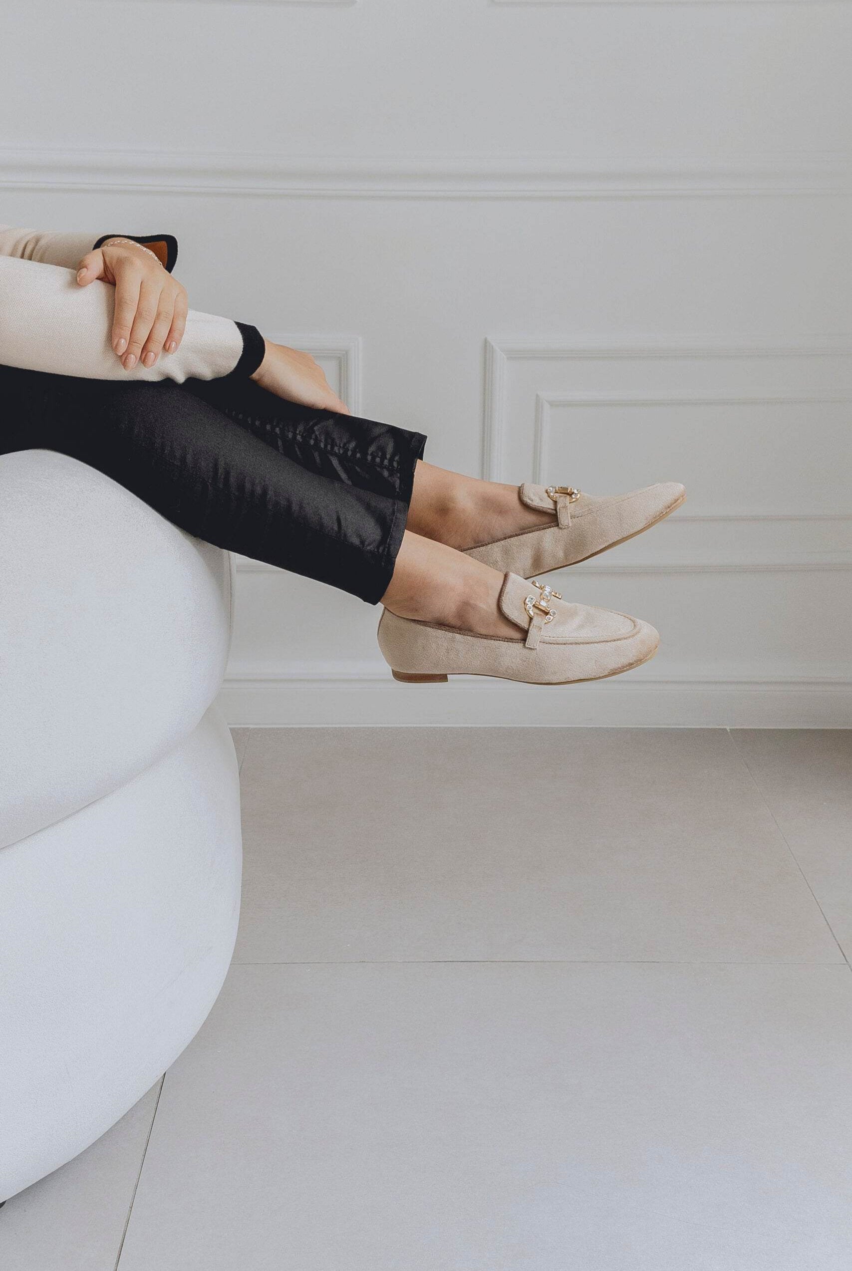 Person wearing beige loafers sitting on a white chair with a neutral background