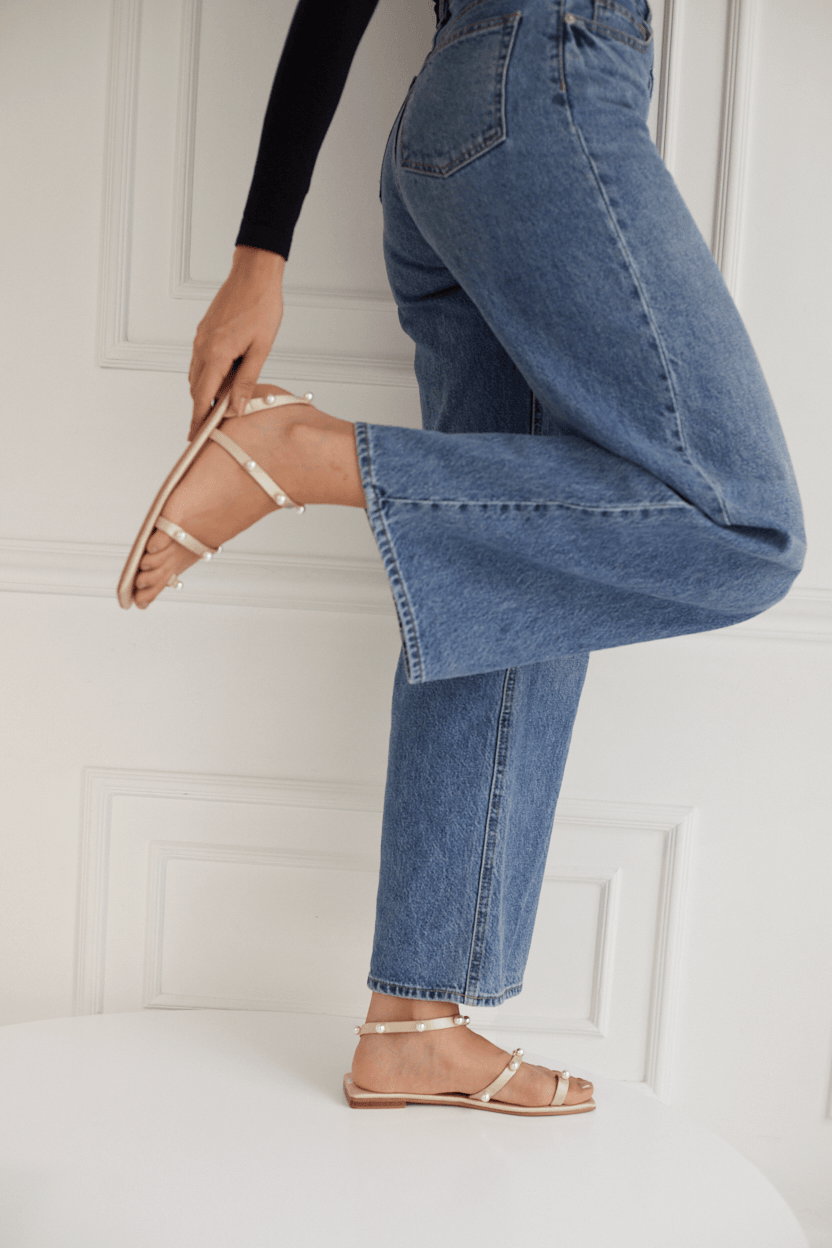 Person wearing blue jeans and strappy sandals with pearls on a white background