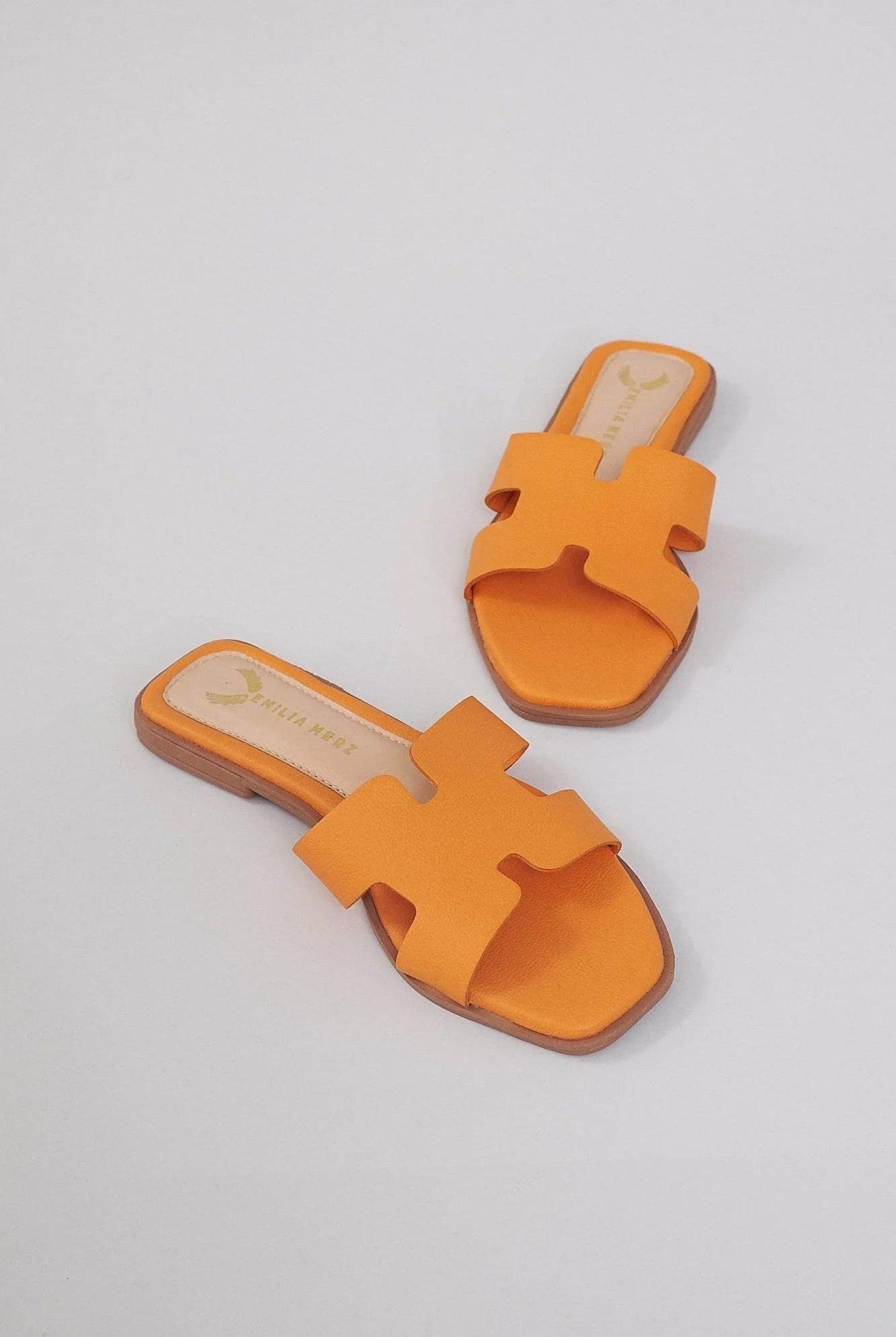 Pair of orange H-shaped slide sandals with open toe and flat sole on a light background