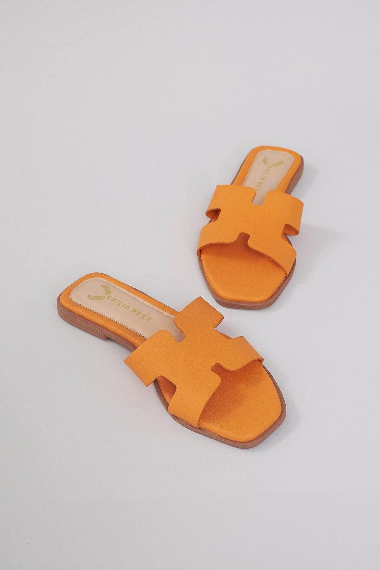 Pair of orange H-shaped slide sandals with open toe and flat sole on a light background