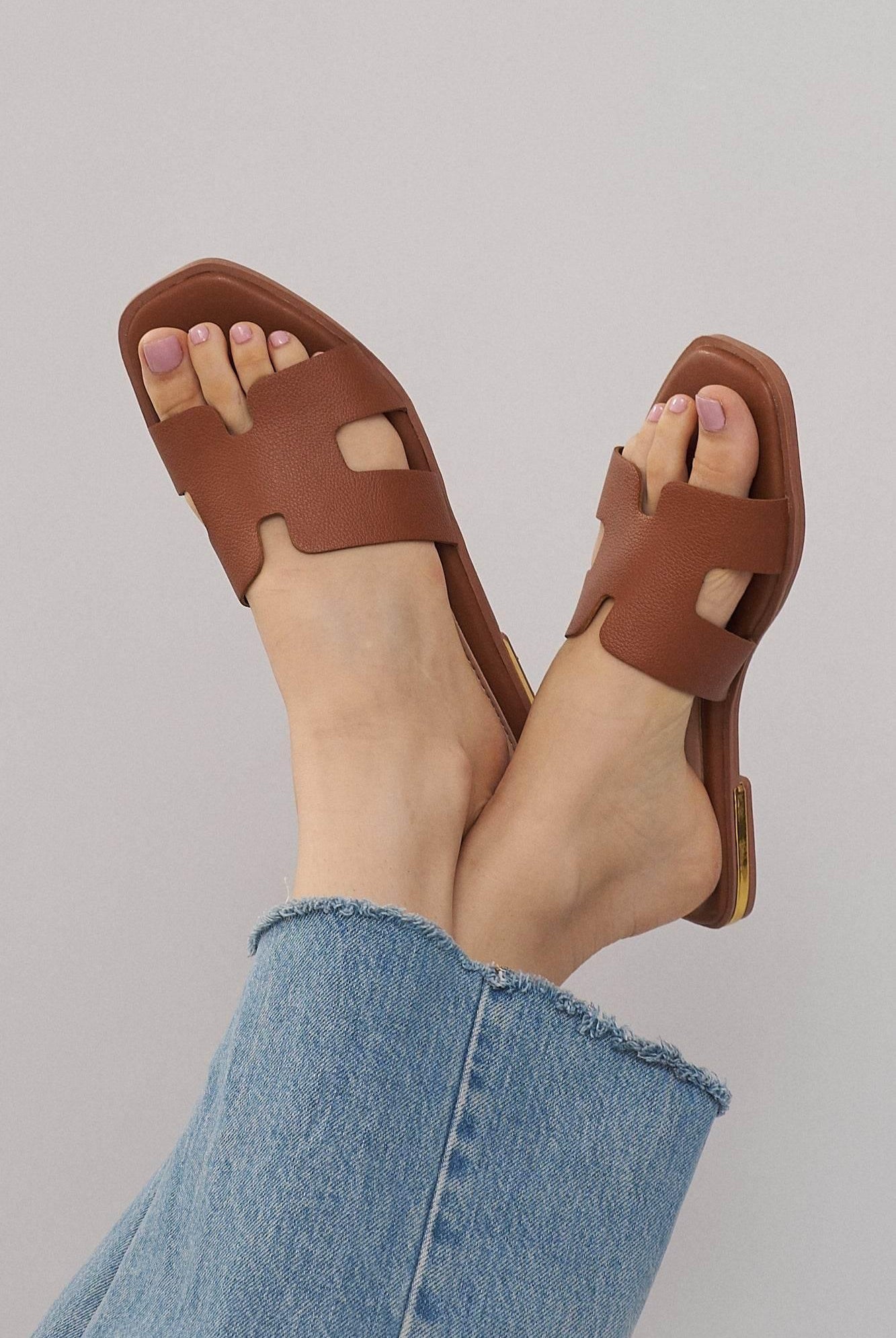 Brown leather flat sandals with cutout design worn with frayed hem jeans
