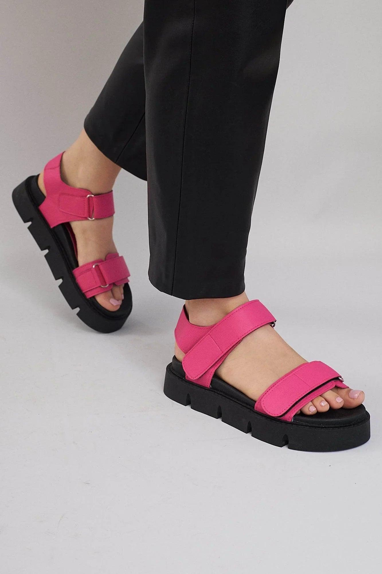 Woman wearing bright pink platform sandals with thick black soles and black pants