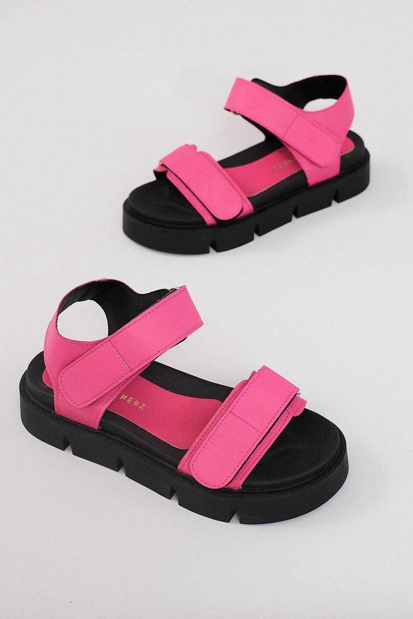 Chunky platform sandals in bright pink with velcro straps and black soles on white background