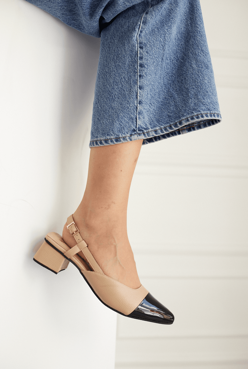 Beige and black pointed-toe shoes worn with blue jeans on a light background