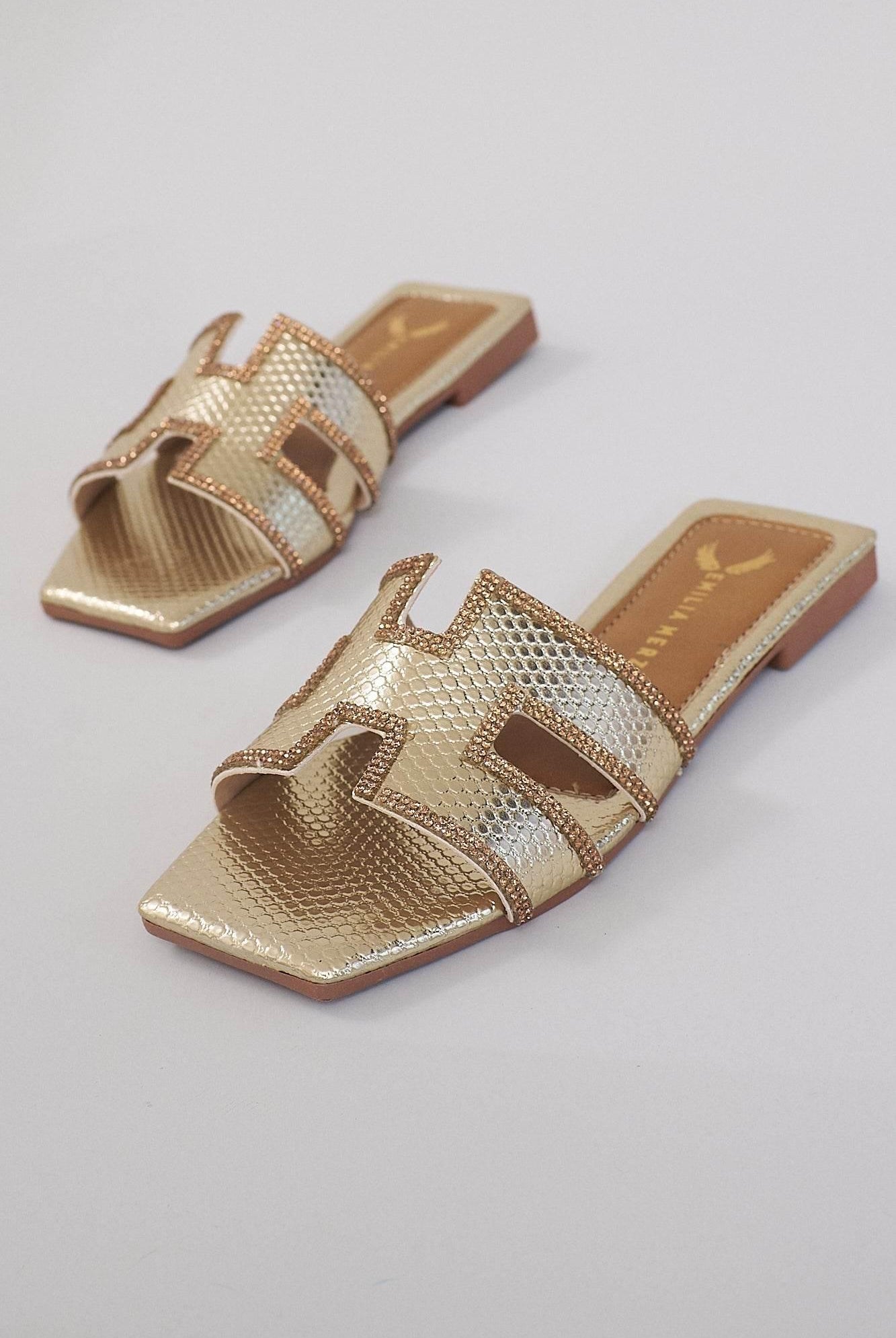 Pair of gold textured slip-on sandals with H cutout design, square toe, and low heel on white background