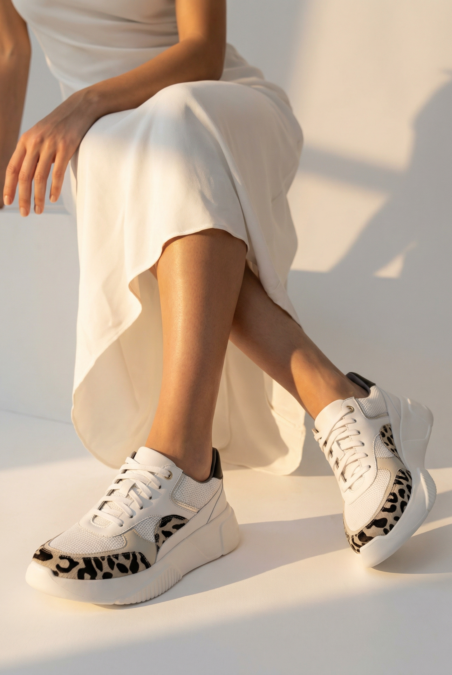 Person wearing white sneakers with leopard print details on a white surface