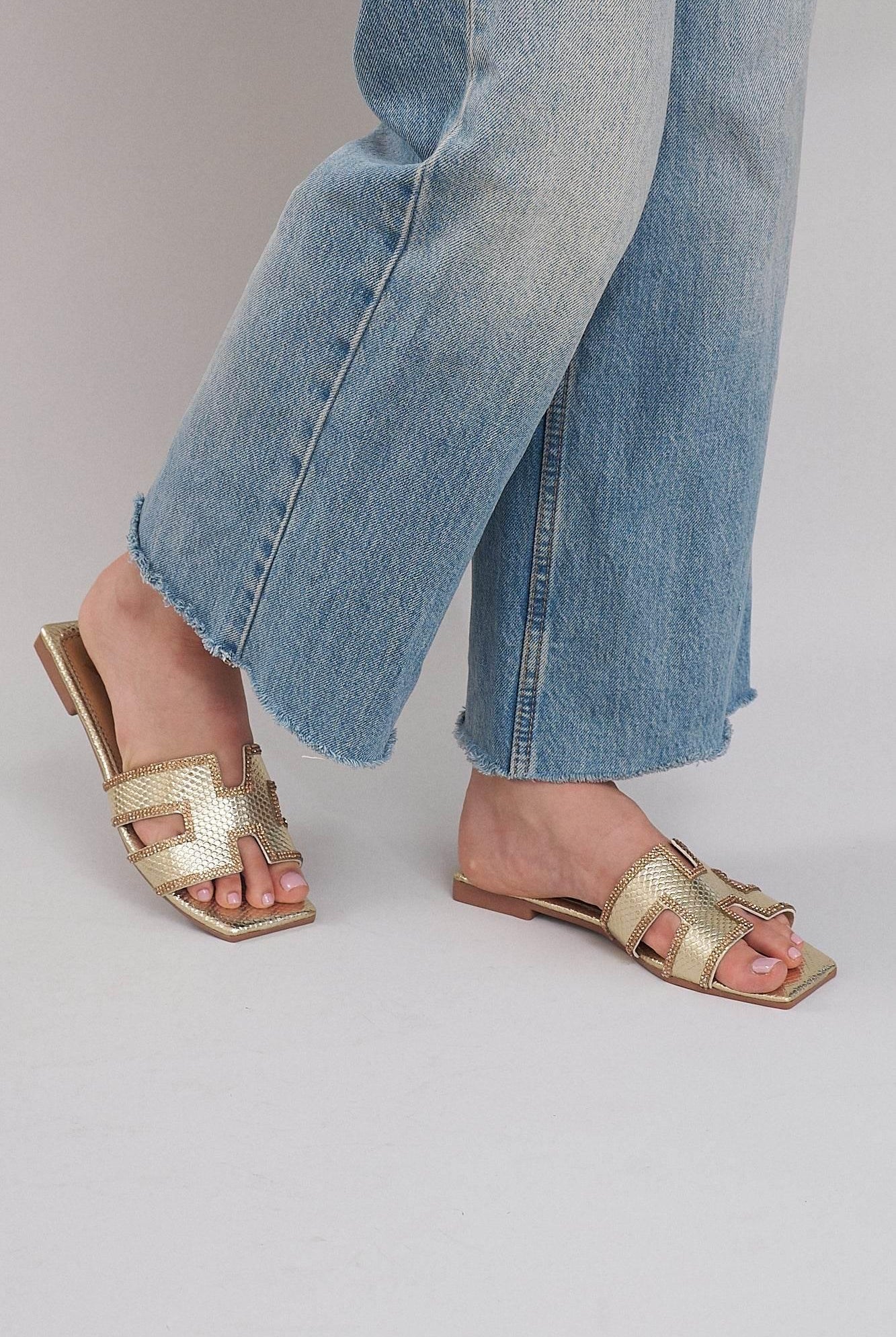 Gold flat sandals with cutout design worn with cropped blue jeans