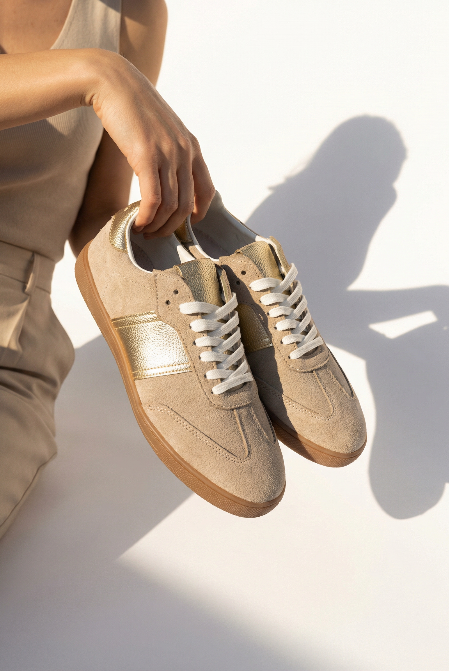 Beige sneakers being held by a person on a light background