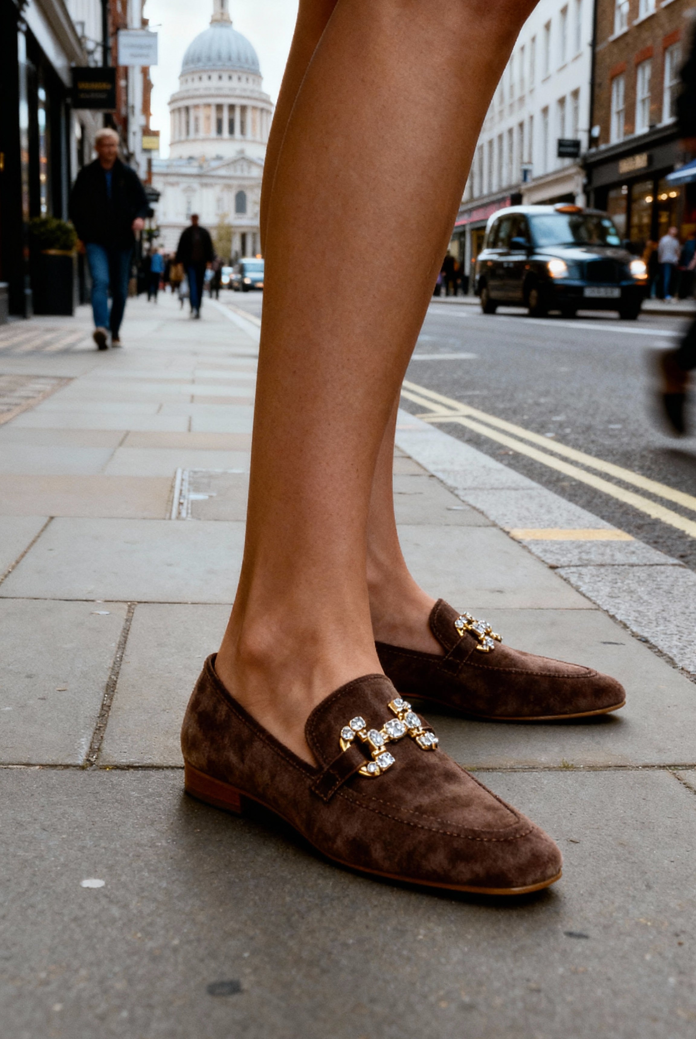 Brown loafers with gold accents worn on a city street.