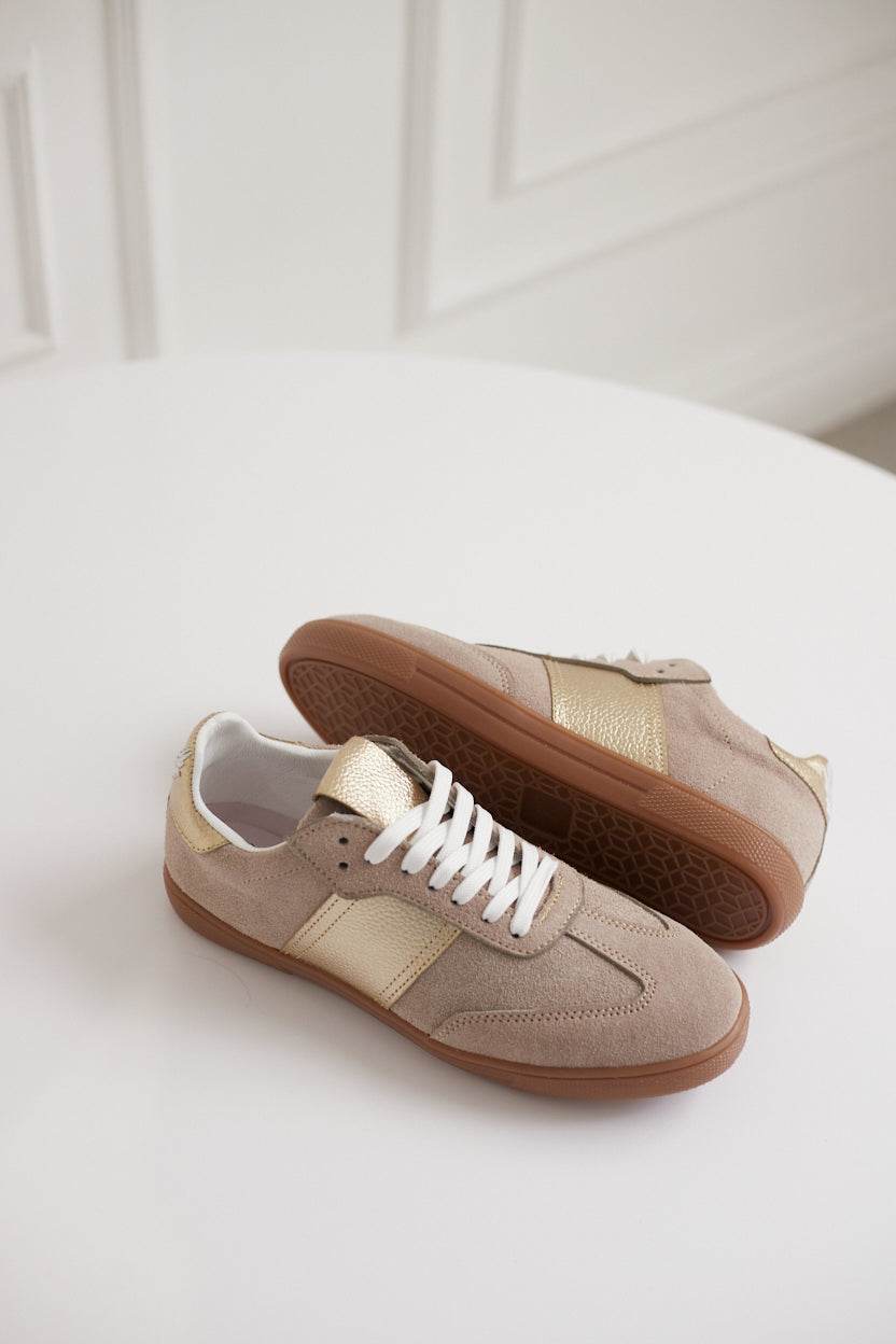 Pair of beige sneakers with white laces on a light background