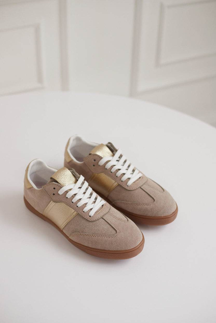 Pair of beige sneakers with white laces on a light background