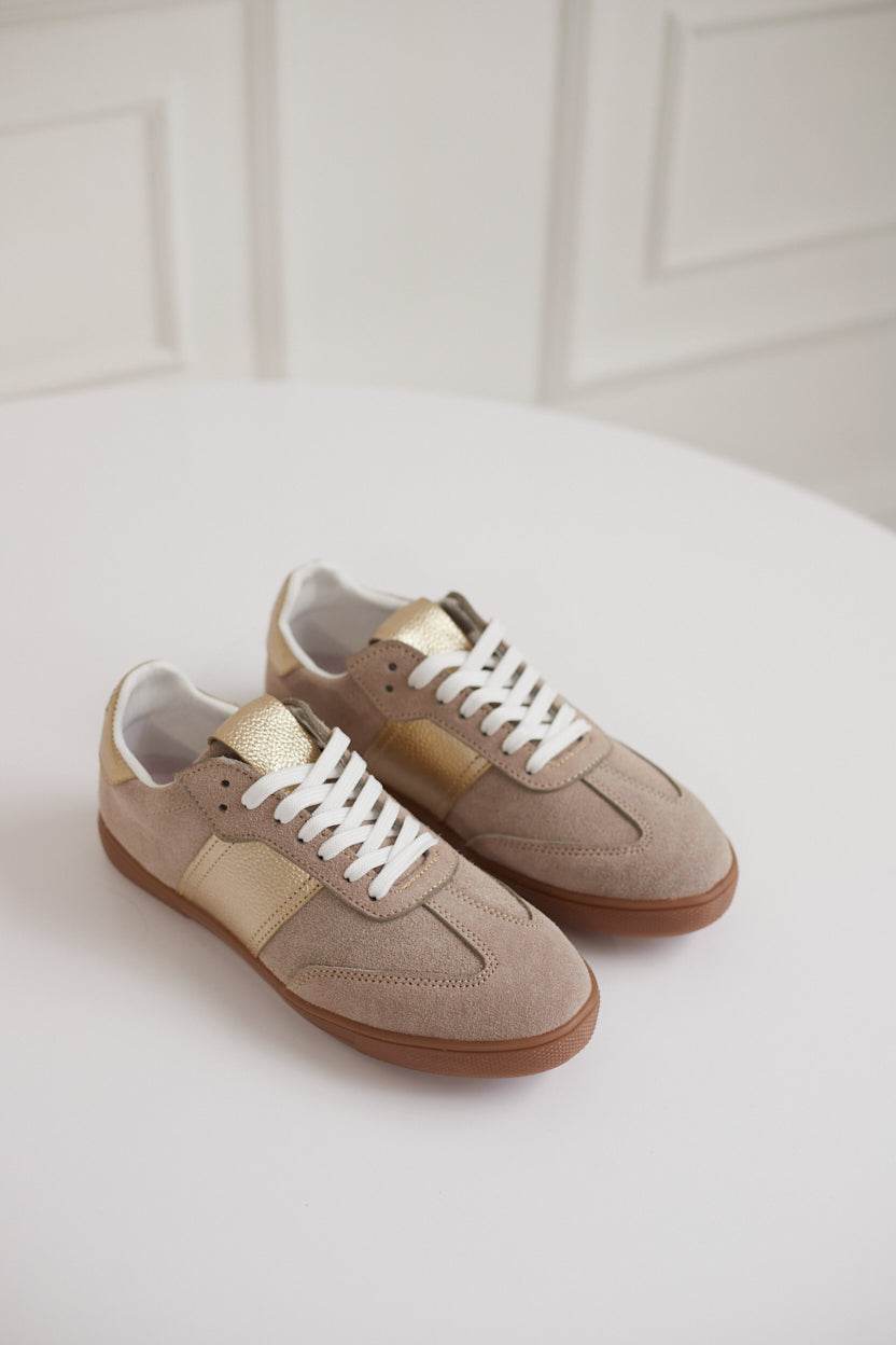 Pair of beige sneakers with white laces on a light background