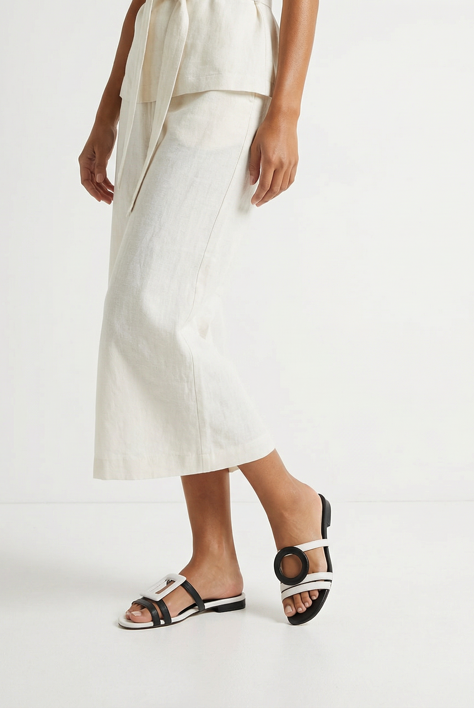 Person wearing a white outfit with asymmetrical sandals on a plain background