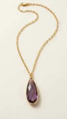 Golden aurea drop necklace with purple gemstone on a beige background