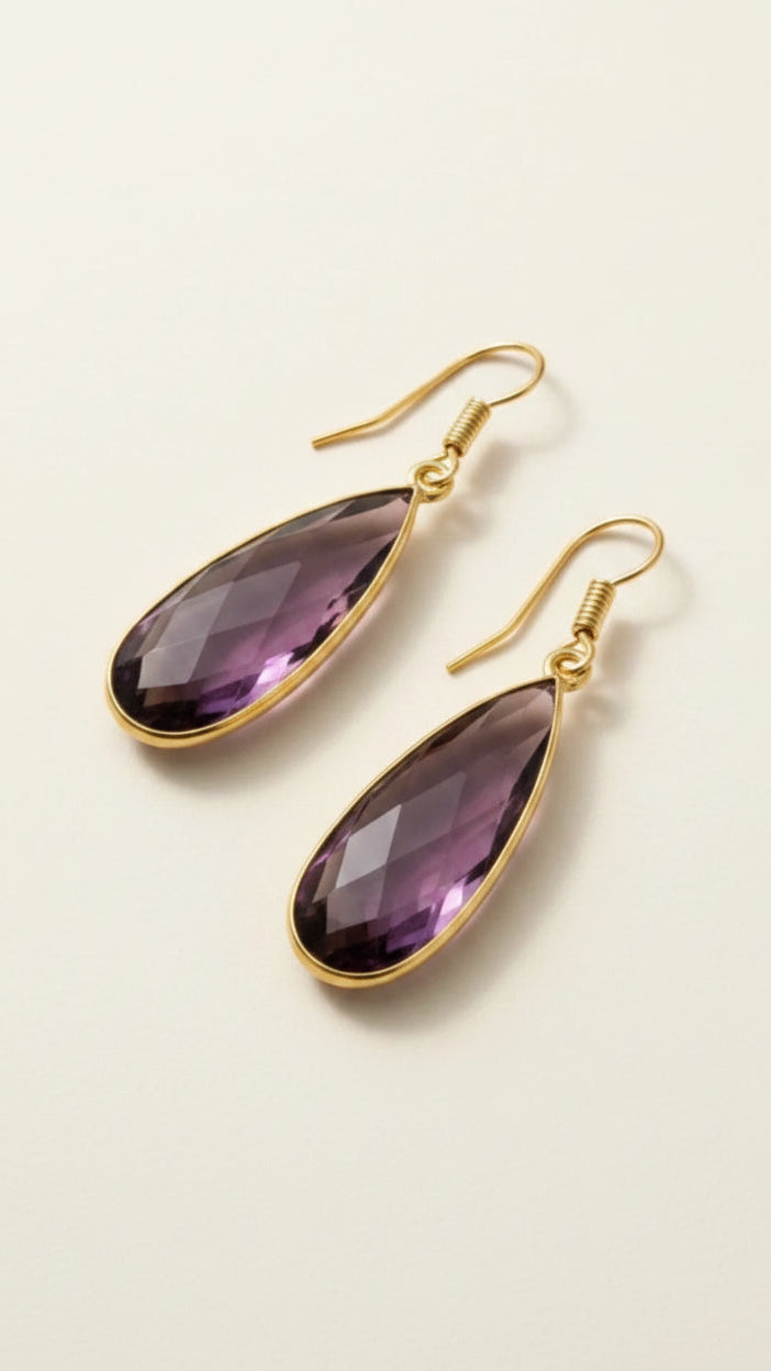 Gold aurea drop earrings with deep violet gemstones on a beige background