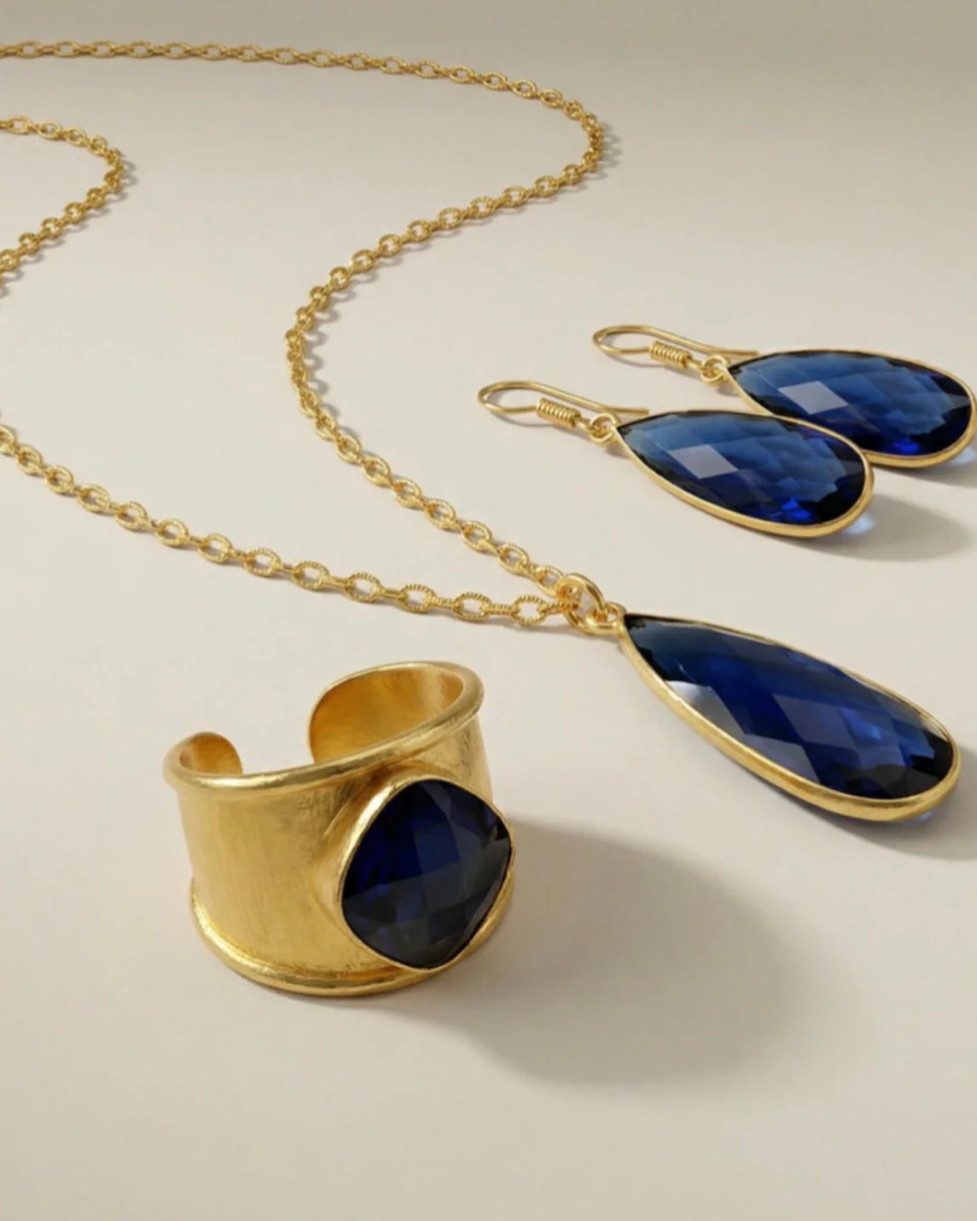 The Aurea statement necklace displayed alongside the matching Emilia Merz drop earrings and ring, showcasing the complete midnight blue jewelry set.