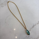 Gold necklace with a green teardrop pendant on a marble surface