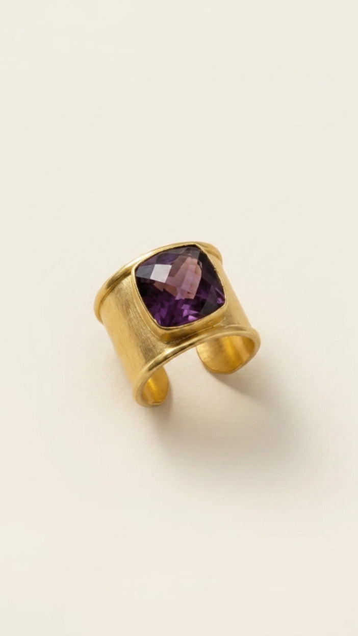 Gold aurea ring with deep violet gemstone on a beige background