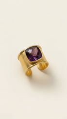 Gold aurea ring with deep violet gemstone on a beige background