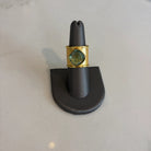 Gold aurea ring with a green gemstone on a black stand against a light gray background
