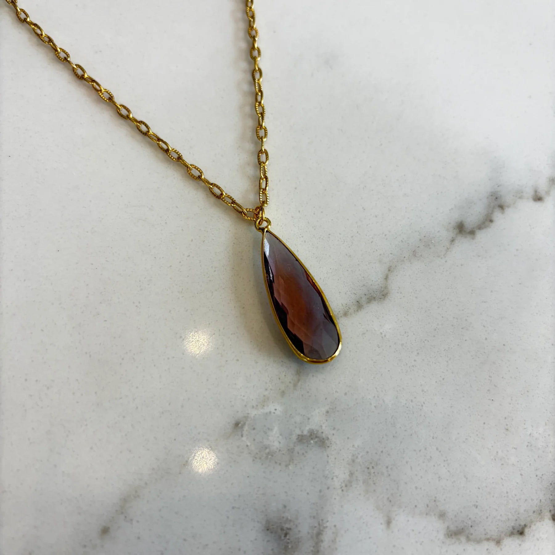Close-up of the Aurea deep violet pendant necklace, highlighting the detailed facets of the gemstone and the polished gold setting.
