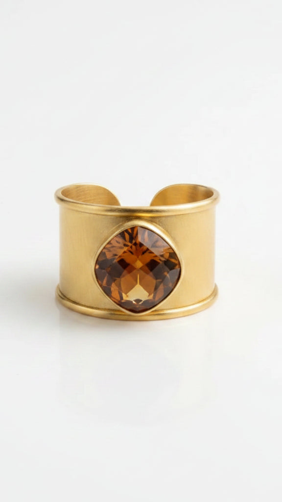 Close-up of the Emilia Merz Aurea Golden Amber statement ring on a display stand, highlighting the wide, textured 18K gold-plated band and the beautiful faceted center stone.