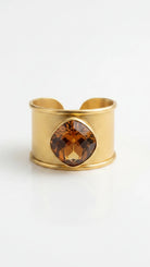 Close-up of the Emilia Merz Aurea Golden Amber statement ring on a display stand, highlighting the wide, textured 18K gold-plated band and the beautiful faceted center stone.