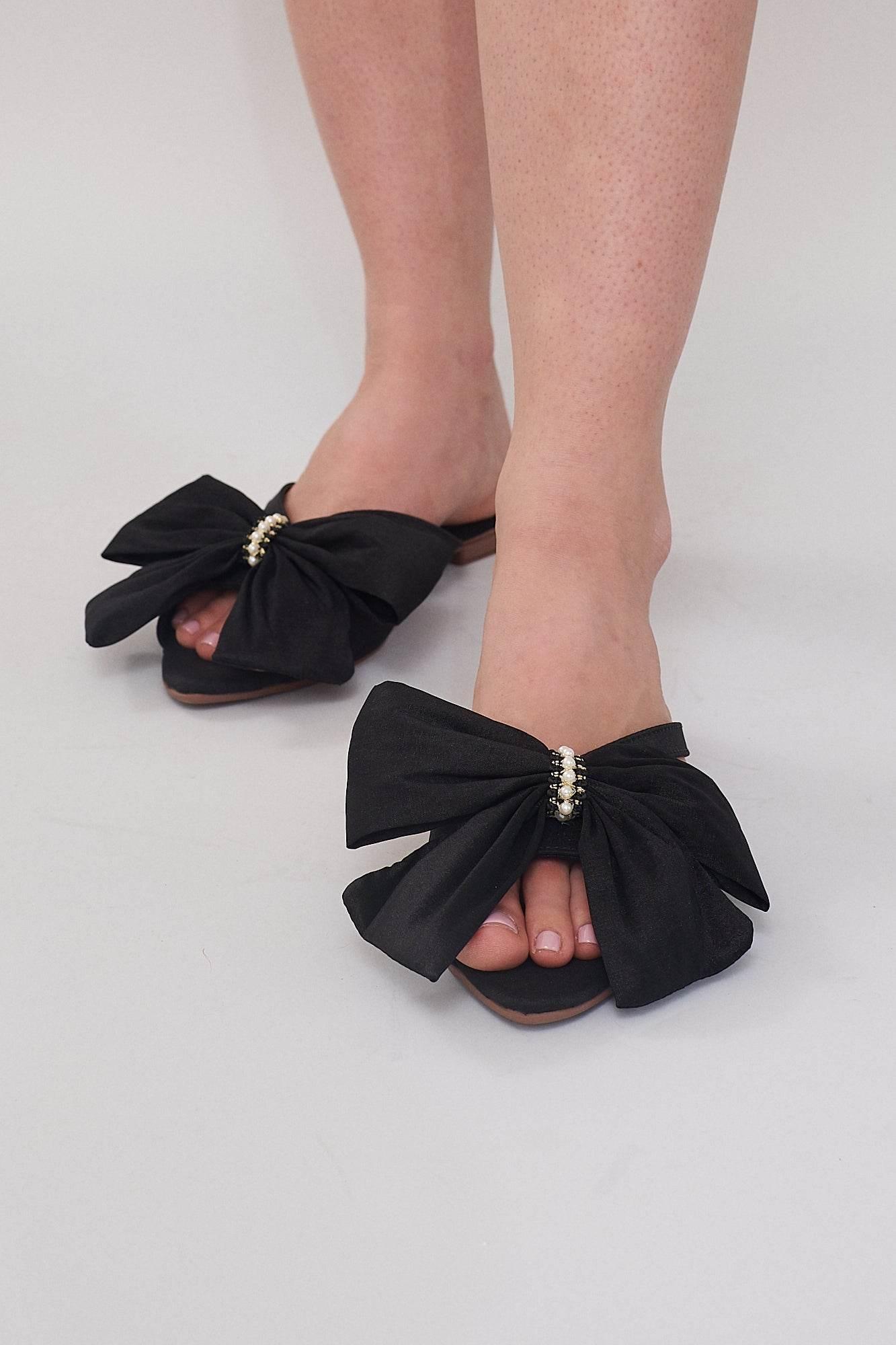 Comfortable black flat sandals for women with statement bow and pearl detailing.