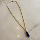 Gold necklace with a blue pendant on a marble surface