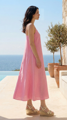 Woman in a pink dress standing by a pool with ocean view