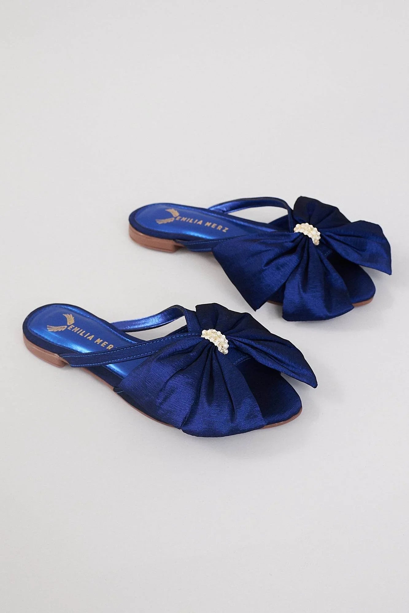 Navy blue flats with large satin bows and pearl embellishments on a neutral background.